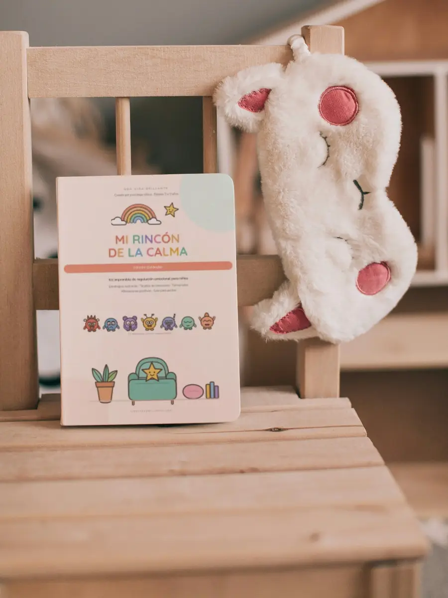 El kit Mi Rincón de la Calma impreso, apoyado en una silla de madera junto a un peluche, en la habitación de un niño.